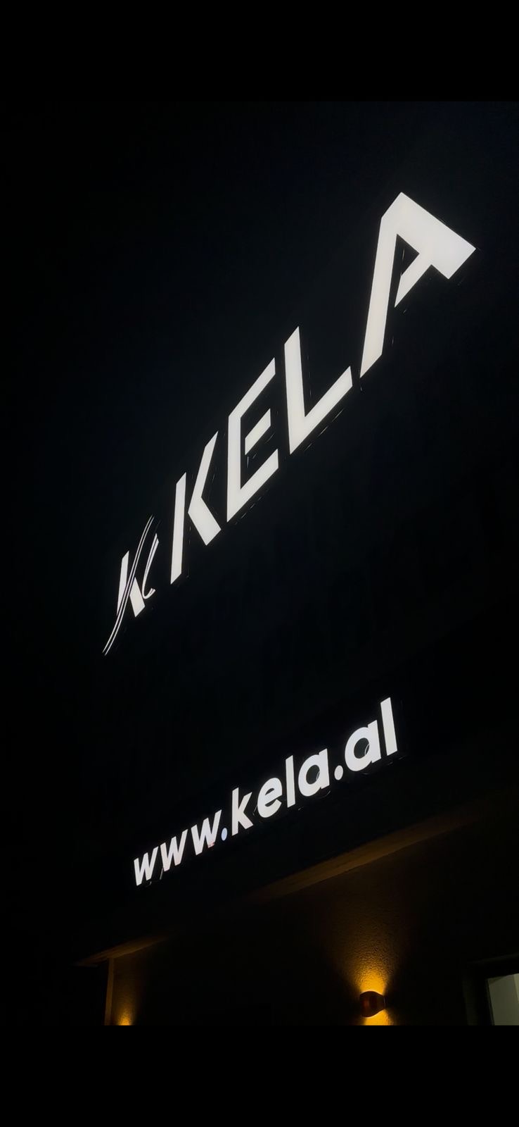 White KELA channel letters glowing at night on a building facade