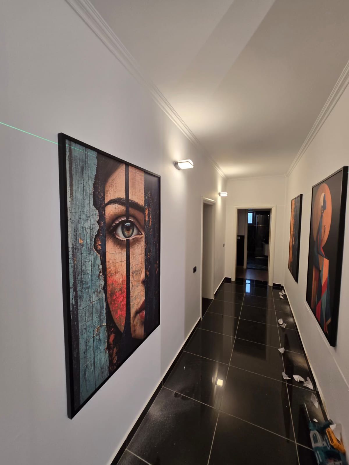 Framed prints being placed in a hallway with a laser line on the wall