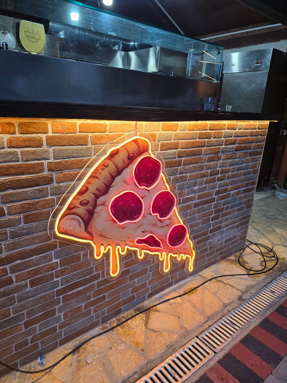 LED neon sign shaped like a pizza slice on a brick counter front