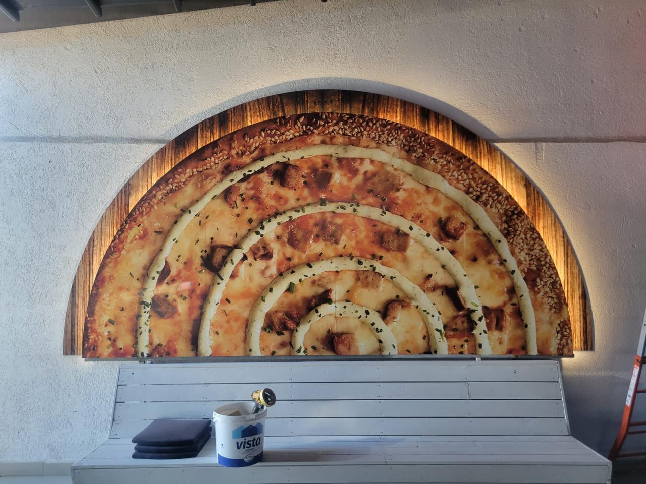Semicircular panel printed with a giant byrek in a wood-look frame, backlit above the white bench
