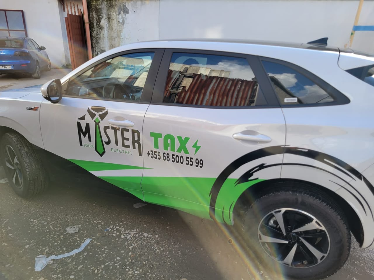 Electric taxi with green and black Mister Taxi graphics, a necktie logo and the phone number on the door