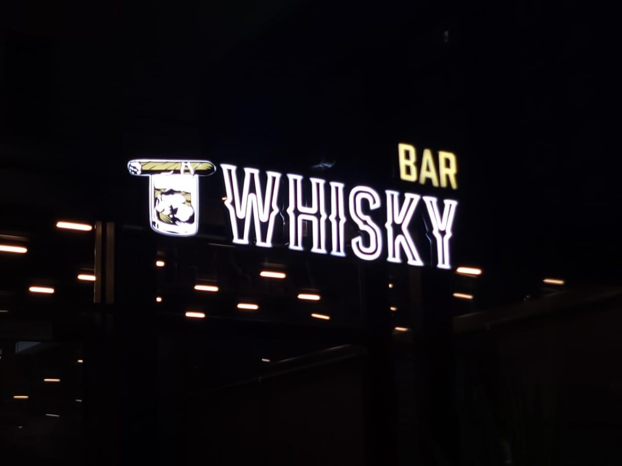WHISKY letters in white neon outline with BAR in yellow and a glass-and-cigar icon, at night
