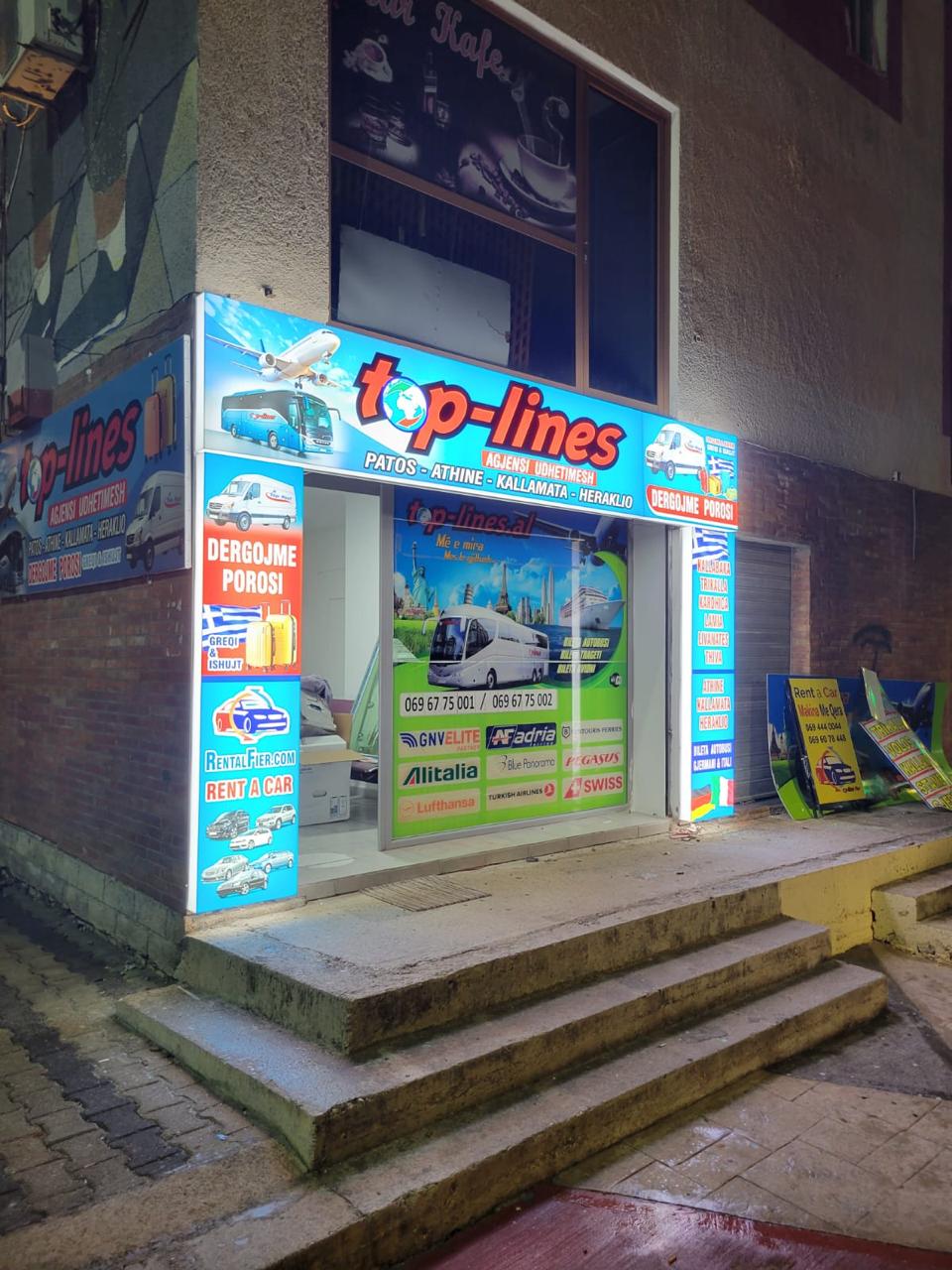 Corner facade of the Top-Lines agency with lit lightboxes and window graphics at night