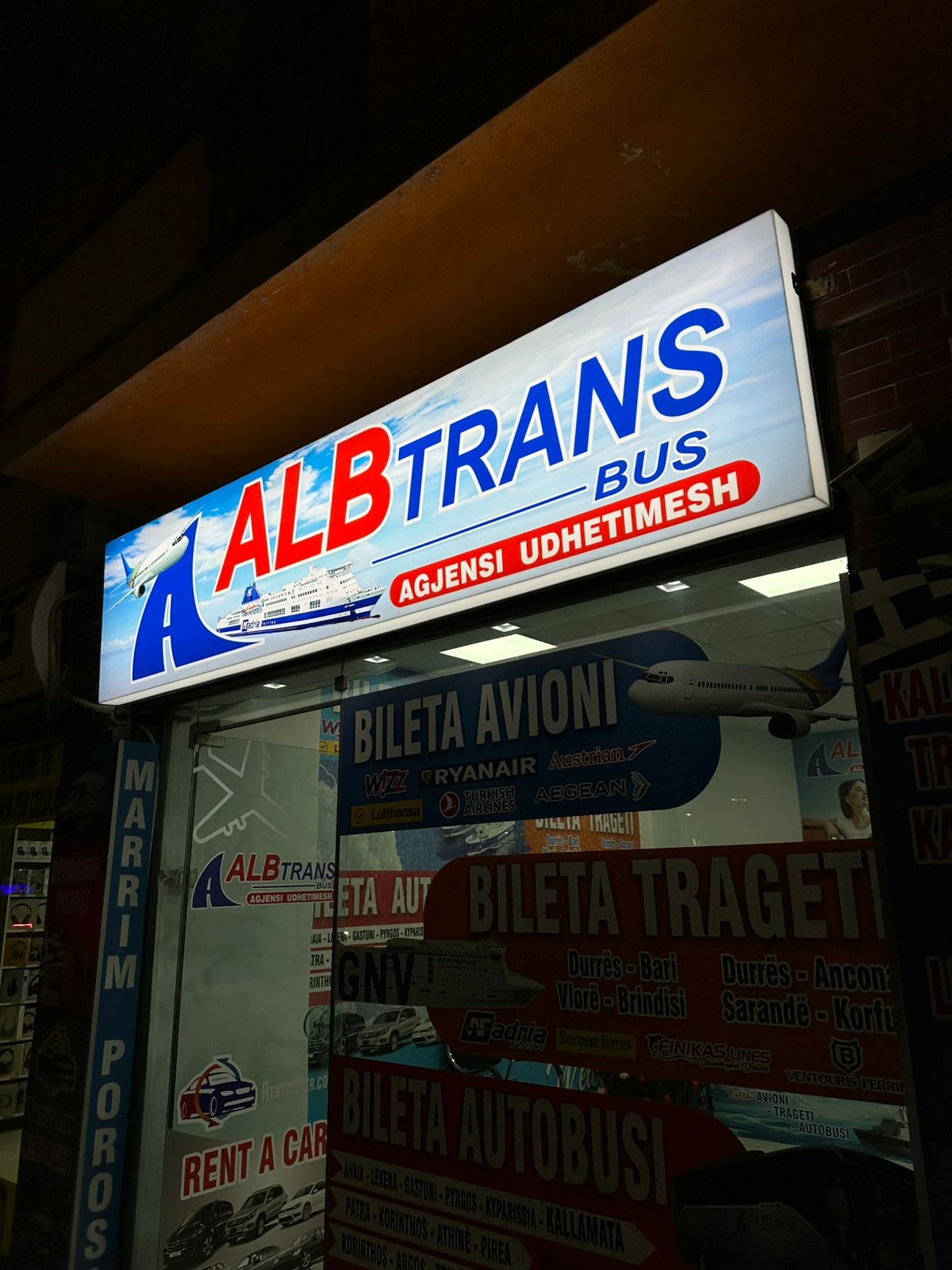 Illuminated AlbTrans Bus agency lightbox at night with ticket graphics on the window