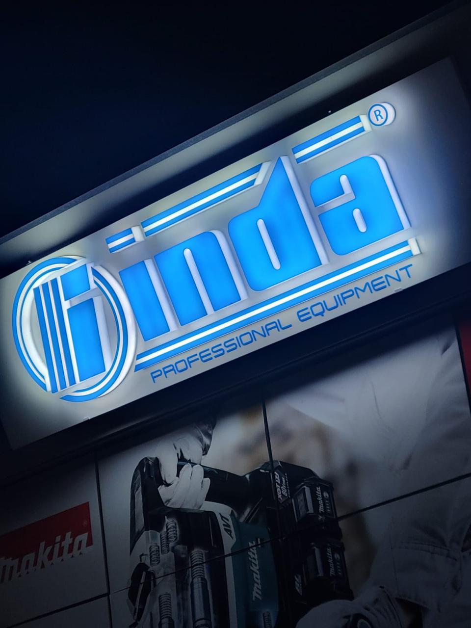 Illuminated blue inda logo letters with a Makita graphic on the tool shop facade at night