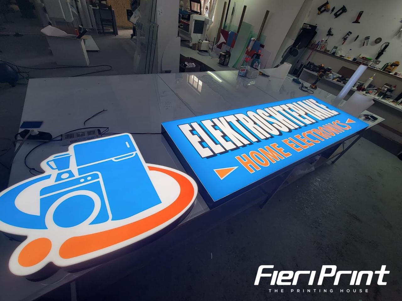 Blue Elektroshtëpiake lightbox and a contour-cut appliance logo sign, lit in the studio