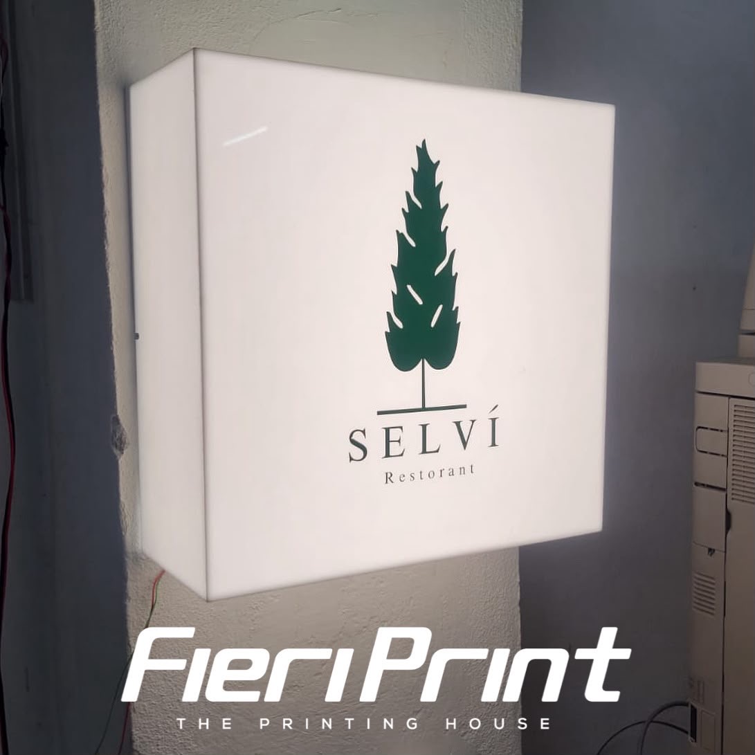White cube lightbox with the green cypress logo for Selví Restorant, lit on the wall